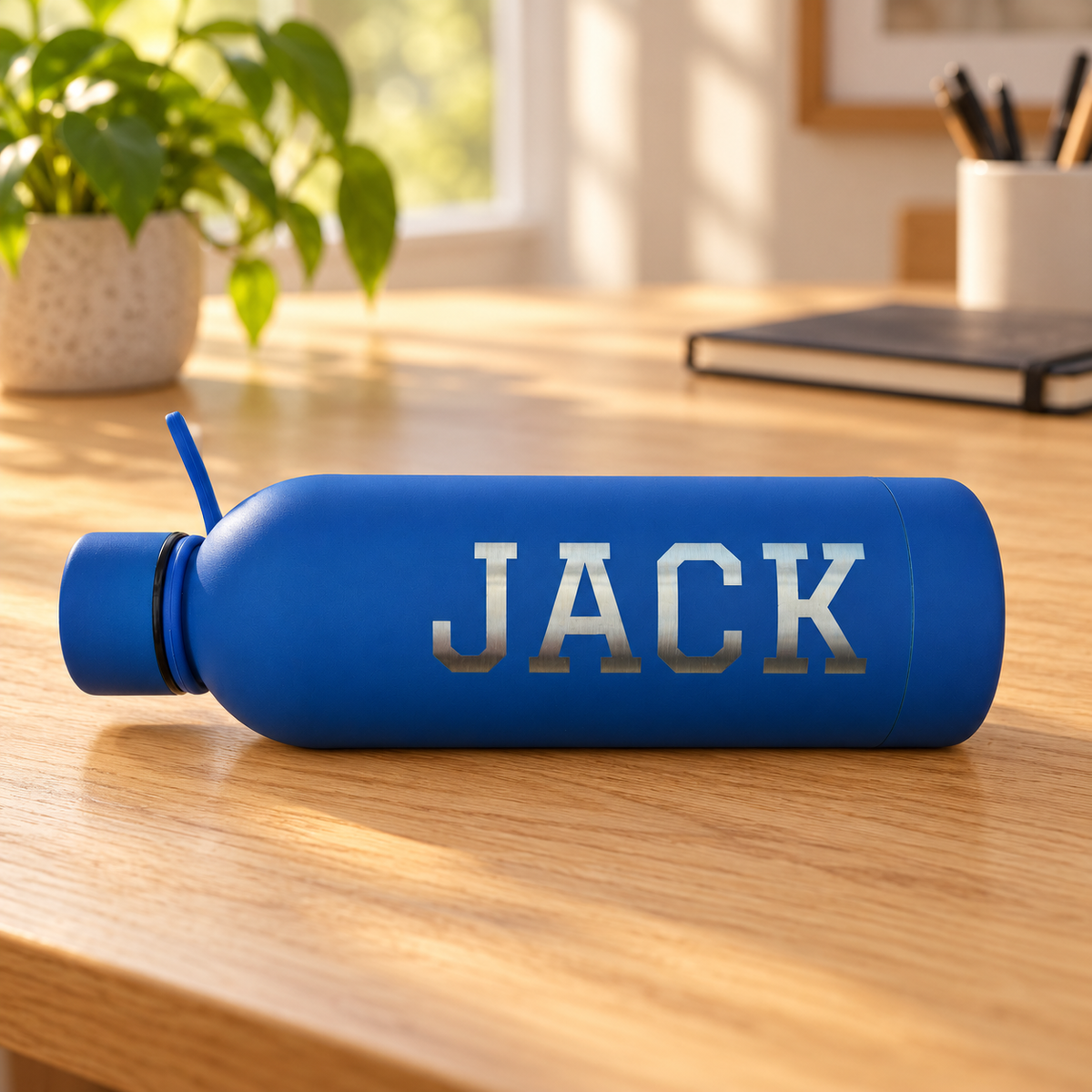 Blue water bottle with JACK engraved in Graduate font on a wooden desk