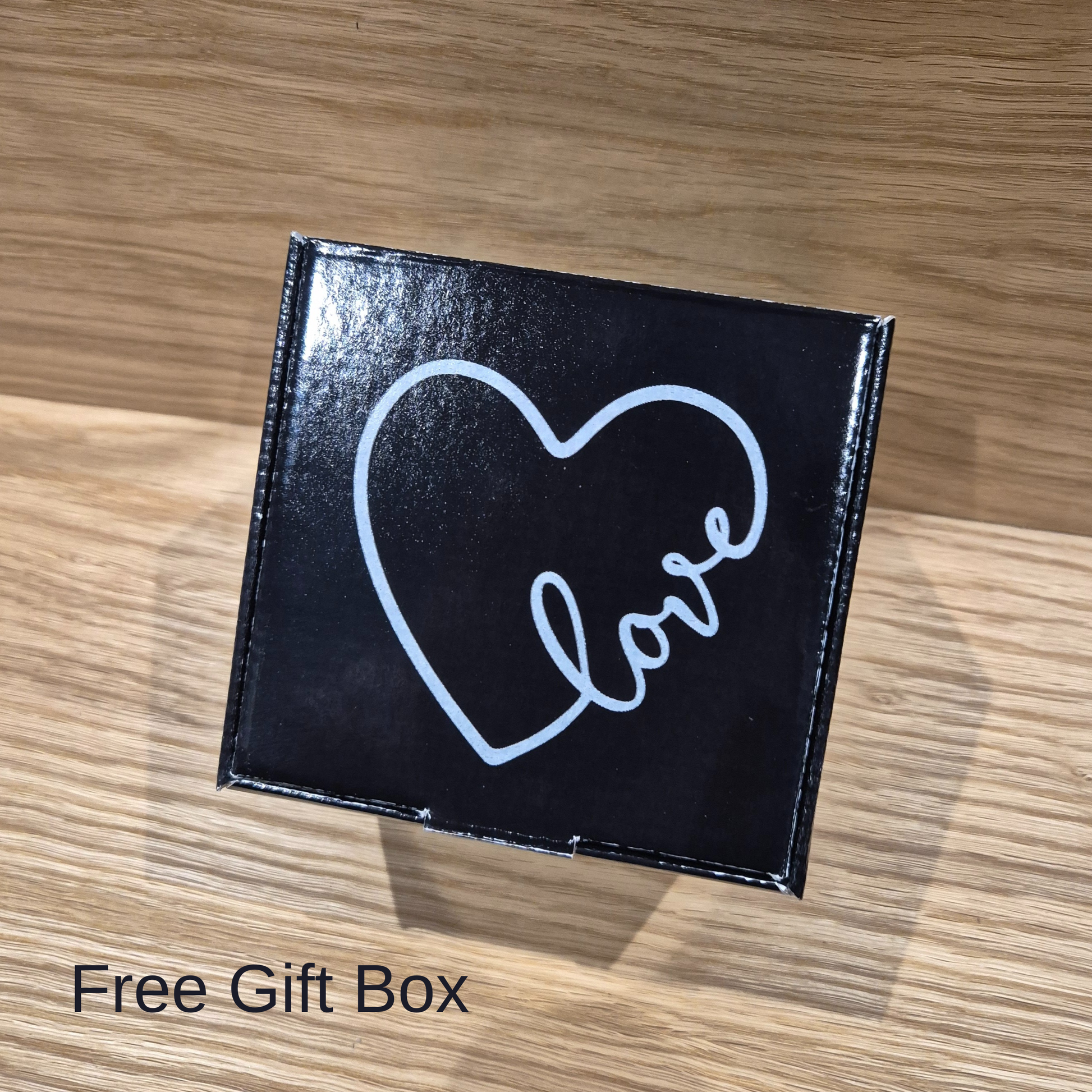 Black square gift box with a white heart and 'love' text on a wooden surface